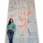 A portrait of the artist against her work, a tall wall painting.